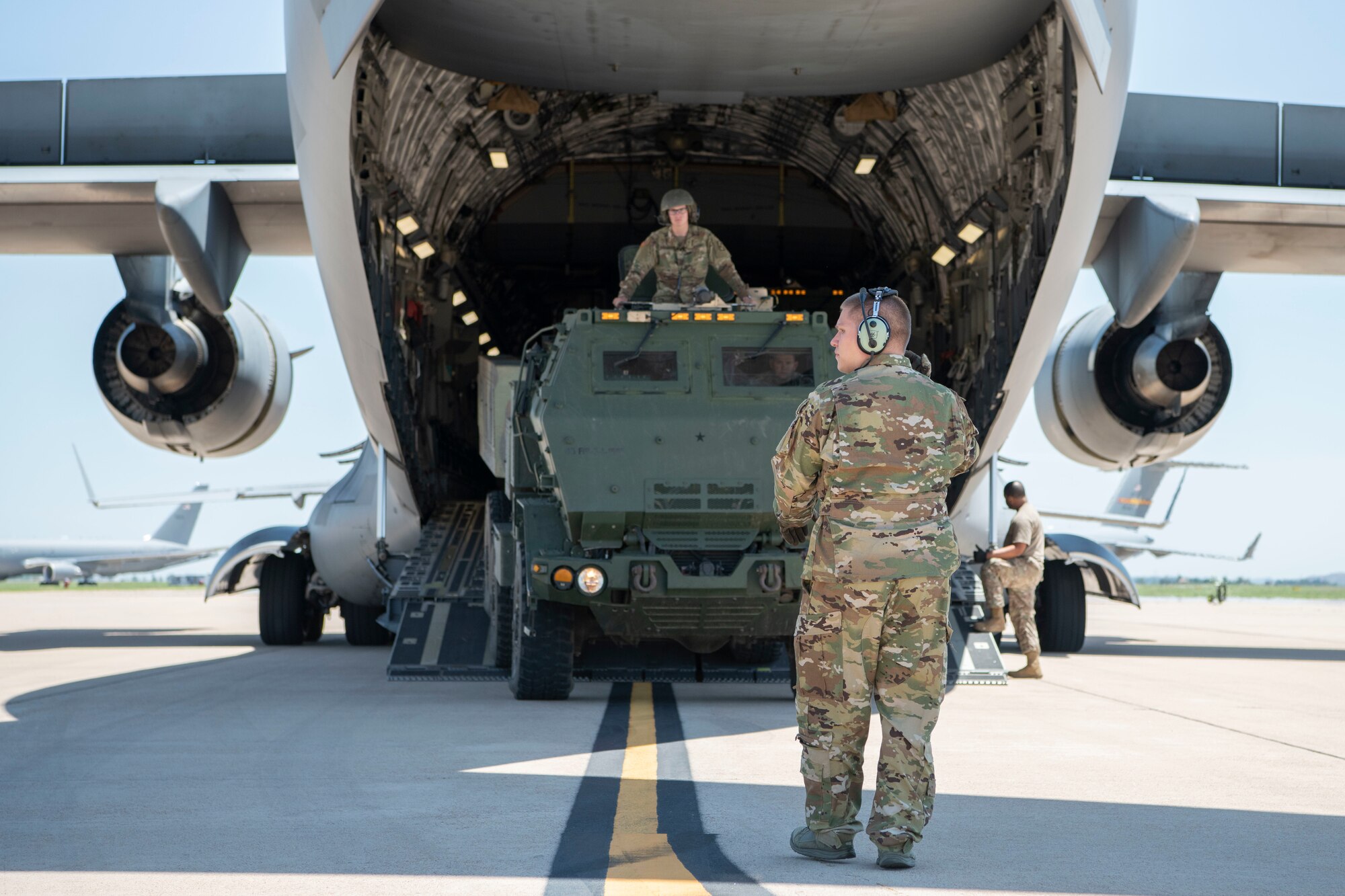 A U.S. Air Force Loadmaster guides a HIMARS off a C-17 Globemaster III.