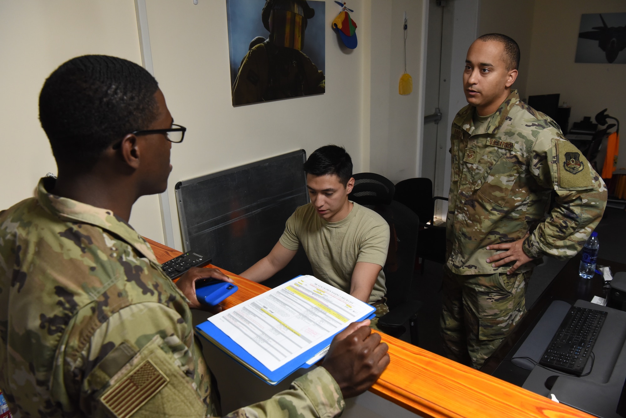 Senior Airman David Gonzalez (center) and Staff Sgt. Alberto Barreto (right), both 380th Air Expeditionary Wing  finance customer service representatives, assist an Airman with in-processing June 6, 2019, at Al Dhafra Air Base, United Arab Emirates.
