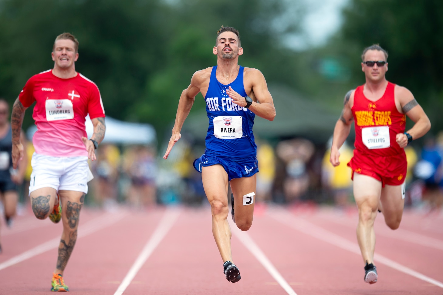 Three male runners sprint down a track, with the background blurred during the 2019 Warrior Games