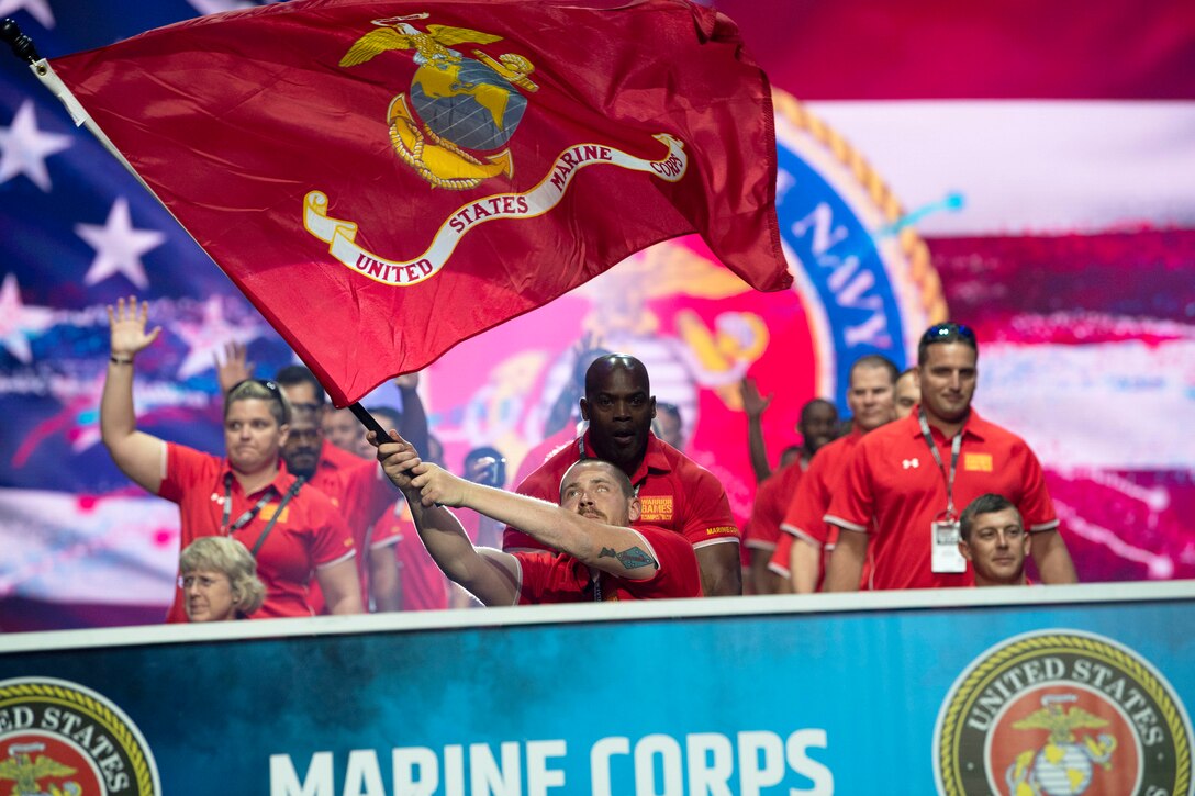 A Marine Corps athlete leading a group of Marine Corps athletes waves a service flag.