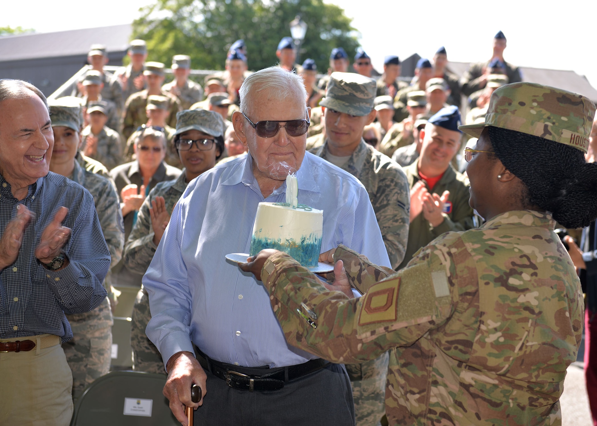 U.S. Air Force Staff Sgt. Amber Houston, right, 100th Logistics Readiness Squadron aircraft parts store supervisor, presents retired Master Sgt. Dewey Christopher, a former 351st Bomb Squadron crew chief, 100th Bomb Group and World War II veteran, a birthday cake as the audience sings “Happy Birthday” to him at the Professional Development Center renaming ceremony on RAF Mildenhall, June 21, 2019. Christopher’s 96th birthday was the weekend after the ceremony, when the PDC was officially renamed the “Dewey R. Christopher Professional Development Center.” (U.S. Air Force photo by Karen Abeyasekere)