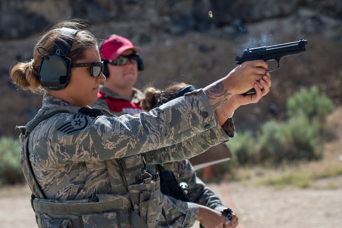 An airman fires a gun while another airman watches.