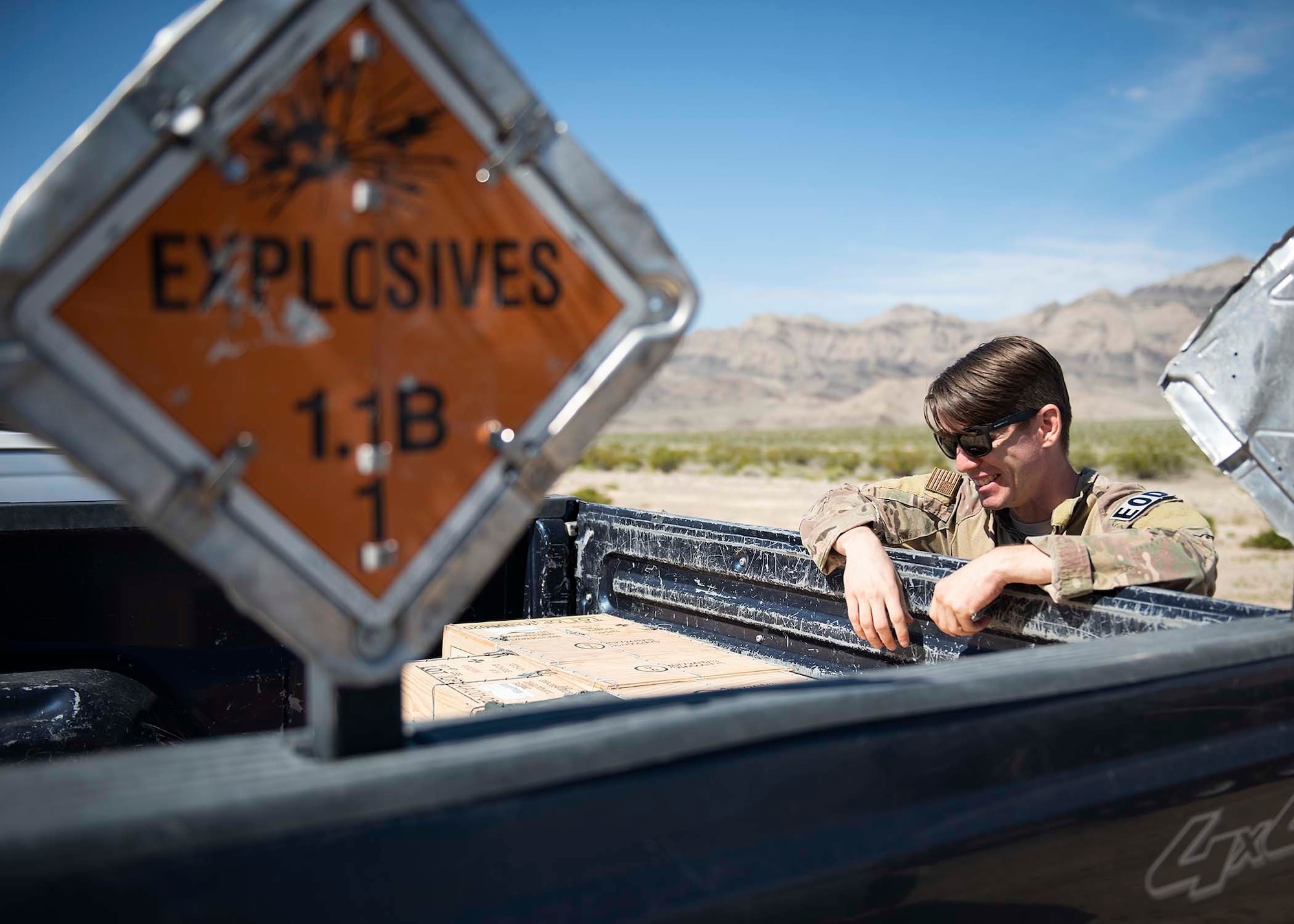 An explosive ordnance disposal technician leans over the back of a truck that contains explosive ordinance.