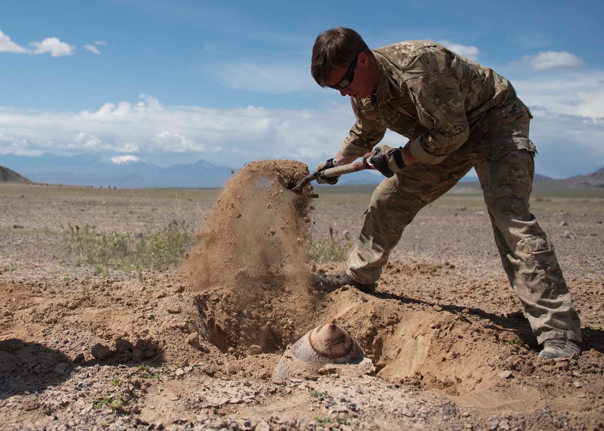 Explosive Ordnance Disposal technician uses a shovel to uncover a berried ordnance.