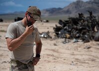 Explosive Ordnance Disposal technician speaks on the radio in front a blown up target.