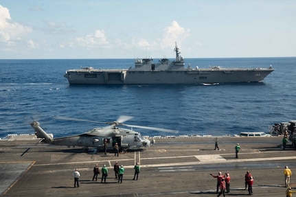 (June 19, 2019) Japan Maritime Self-Defense Force (JMSDF) ship JS Izumo (DDH-183) sails alongside the Navy™s forward-deployed aircraft carrier USS Ronald Reagan (CVN 76) while an MH-60R Sea Hawk from Helicopter Maritime Strike Squadron (HSM) 77 conducts flight operations. Ronald Reagan, the flagship of Carrier Strike Group 5, provides a combat-ready force that protects and defends the collective maritime interests of its allies and partners in the Indo-Pacific region.