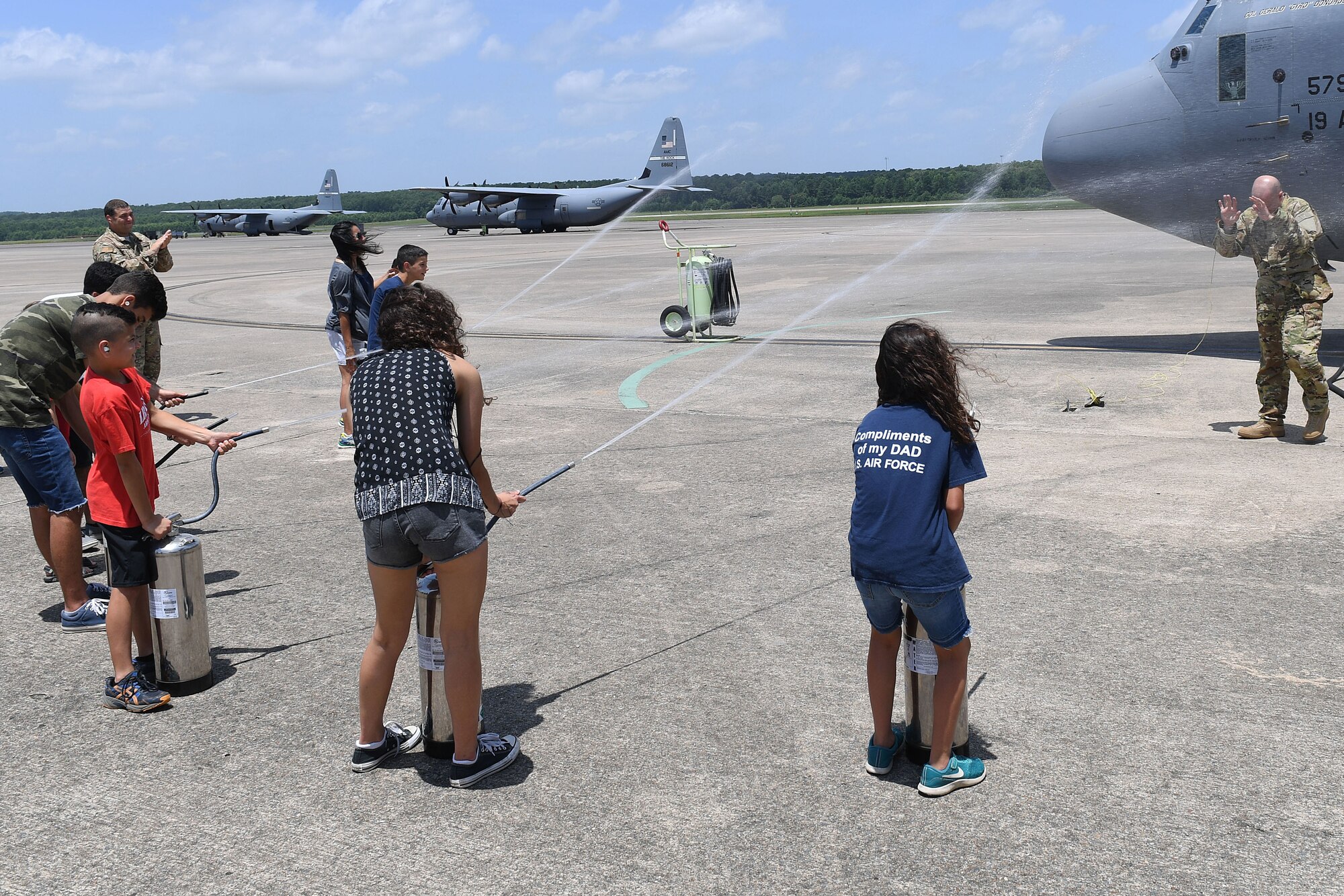 An Airmen is sprayed with a hose by his children after getting off a C-130J
