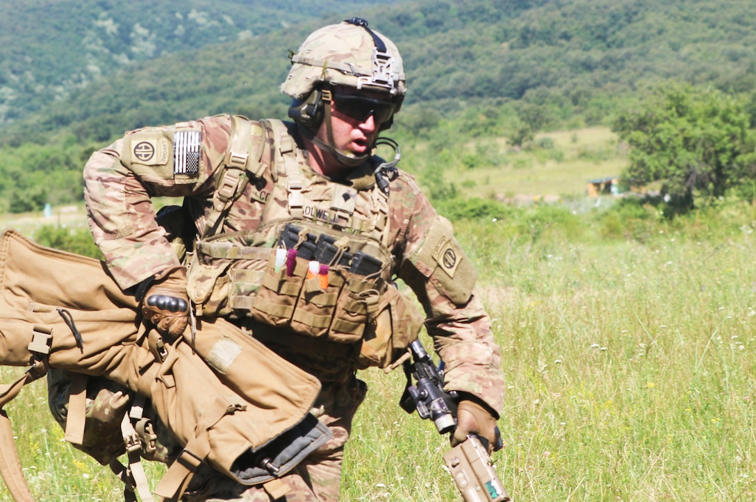 A soldier in combat gear moves quickly while carrying a rifle, a backpack and an extra weapon bag.