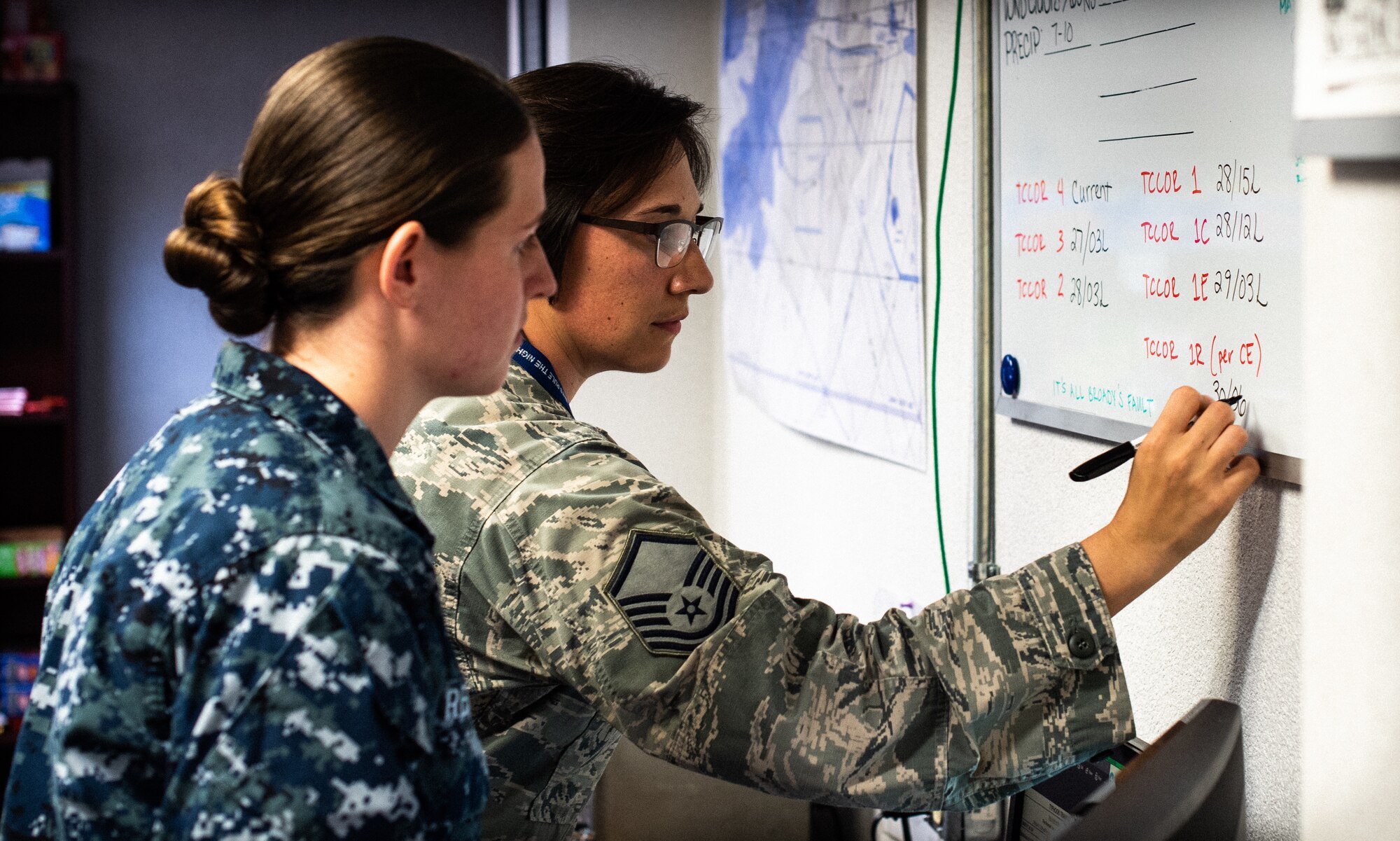 U.S. Air Force Master Sgt. Leah Gonzalez, 18th Operations Support Squadron NCO in charge of airfield support, and U.S. Naval Airman Amber Renchen, an apprentice weather forecaster with the Navy Oceanography and Anti-Submarine Warfare Detachment, work together as members of the Joint Weather Okinawa team monitoring tropical cyclone conditions of readiness.