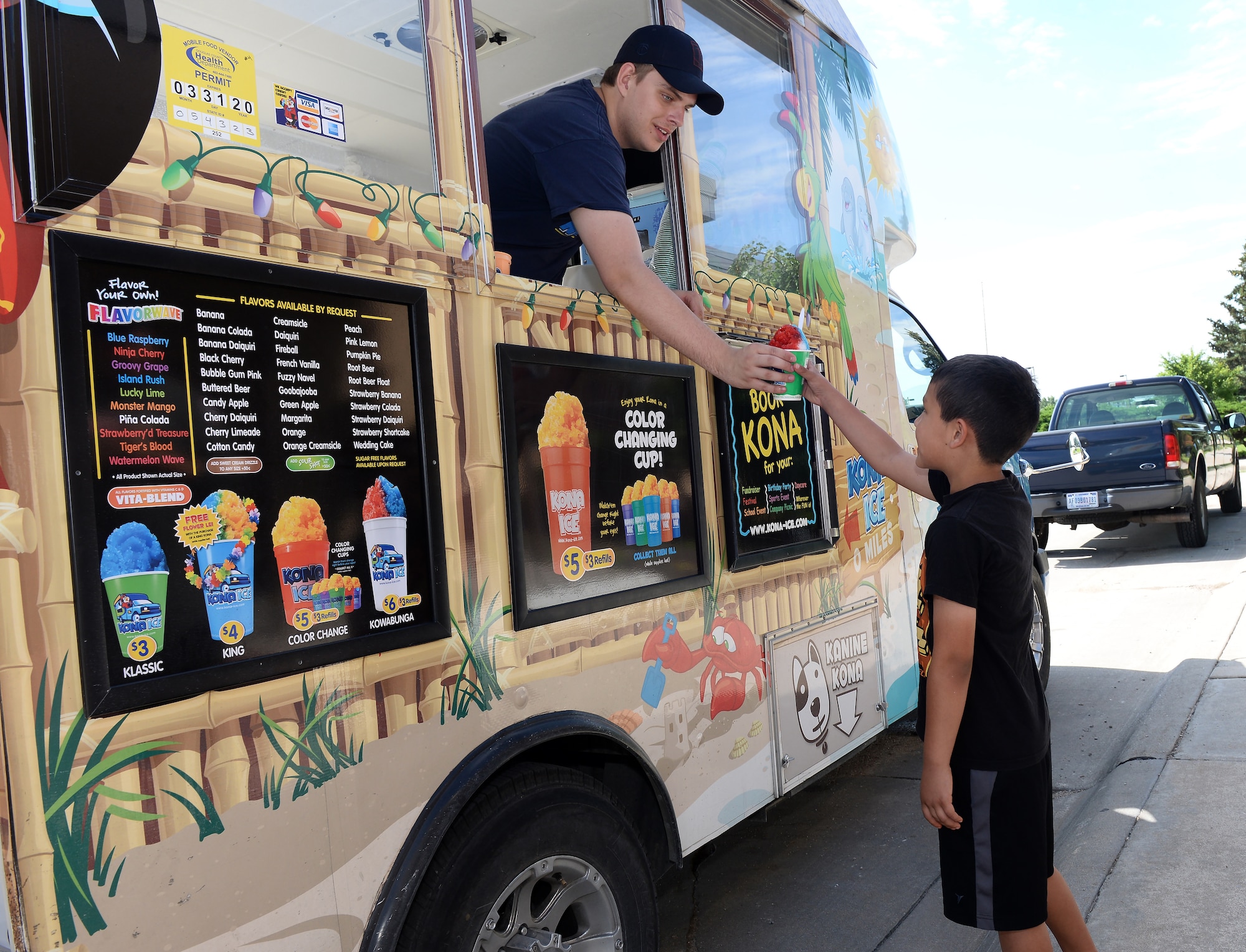 Joel Monteleagre, server with Kona Ice, gives a tropical flavored shaved ice cup to Hosea Sanchez, the son of U.S. Air Force Kevin Sanchez, 343rd Reconnaissance Squadron dot-flight chief, during a morale event June 20, 2019, at the Warhawk Community Center on Offutt Air Force Base, Nebraska. The 55th Wing Chaplain core hosted the events to lift the spirits of member of Team Offutt in the wake of the historic flooding. (U.S. Air Force photo by Charles J. Haymond)