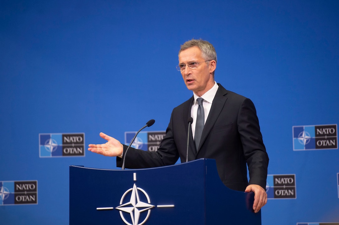 A man in large room speaks at a dias.