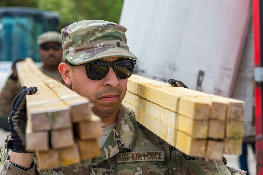 Airman 1st Class Jesse Vega, 23d Civil Engineer Squadron electrical power production engineer, carries timber, May 31, 2019, in Sainte-Mère-Église, France. The engineers provided structural support for the Commemoration of D-Day 75 by repairing and building bridges that were used to access hard-to-reach areas of a parachute drop zone. As part of the commemoration, parachutists from across the Department of Defense performed the same jumps their predecessors did on D-Day. (U.S. Air Force photo by Airman 1st Class Hayden Legg)