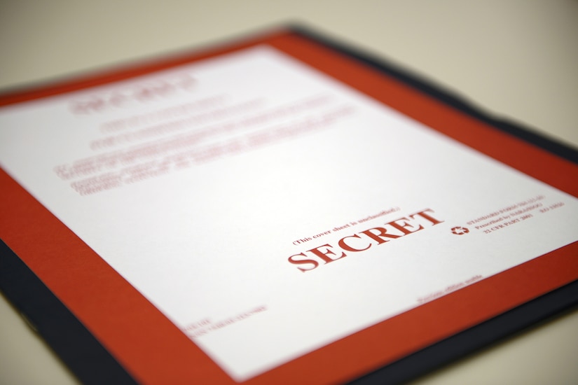 A blue folder bears a red and white cover sheet marked “SECRET.”