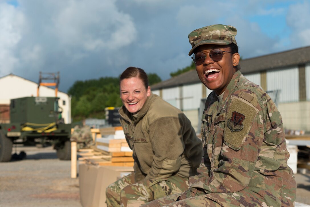 Staff Sgt. Jessica Armond, 23d Civil Engineer Squadron (CES) emergency management logistics NCO in charge, left, and Senior Airman Kamilah Hobbs, 23d CES operations manager, right, laugh, June 5, 2019, in Sainte-Mère-Église, France. The engineers were given unique opportunities such as this incentive flight for repairing and building bridges that were used to access hard-to-reach areas of a parachute drop zone during the Commemoration of D-Day 75. As part of the commemoration, parachutists from across the Department of Defense performed the same jumps their predecessors did on D-Day. (U.S. Air Force photo by Airman 1st Class Hayden Legg)