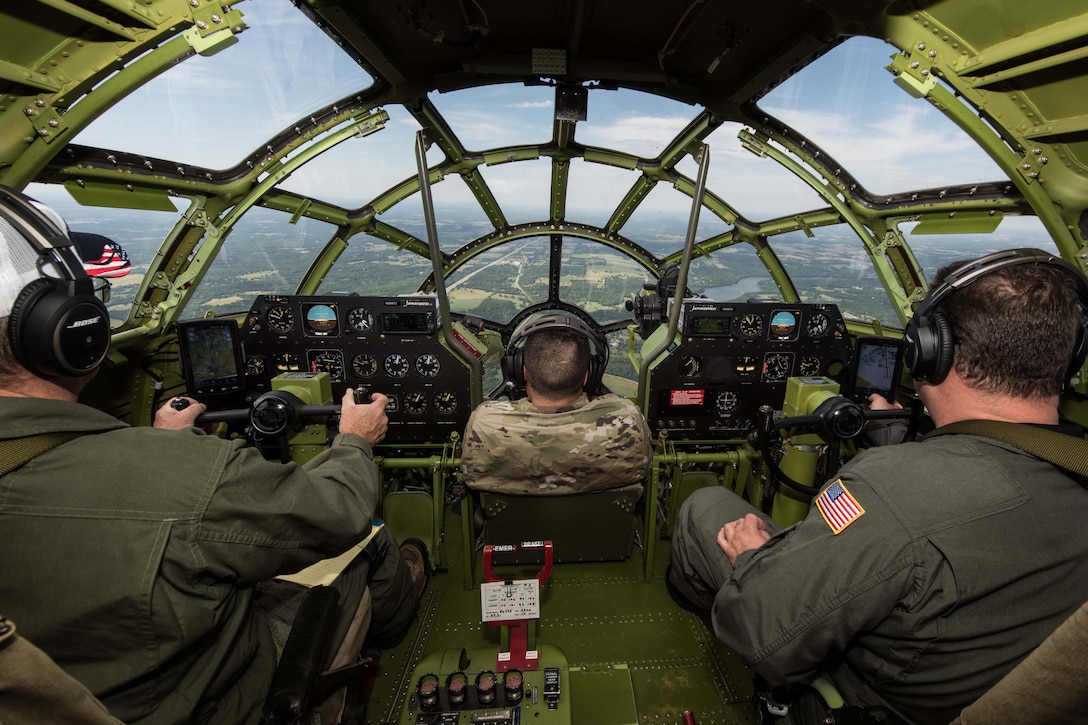 Three people are seen in the cockpit of a b-29 aircraft midair.