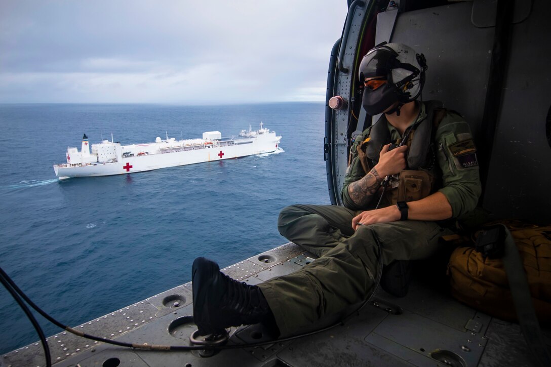 A man in a helicopter looks out over a ship in the ocean.