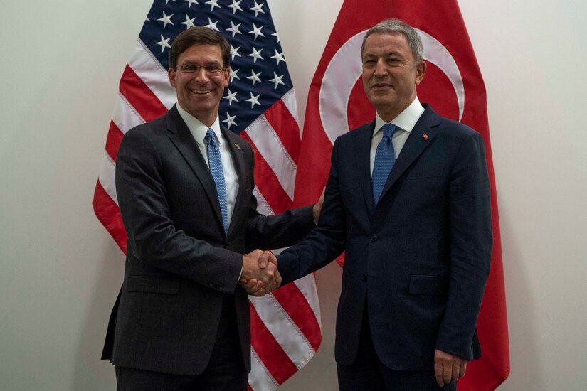 Acting Defense Secretary Mark T. Esper shakes hands with the Turkish defense minister in front of both nations' flags.