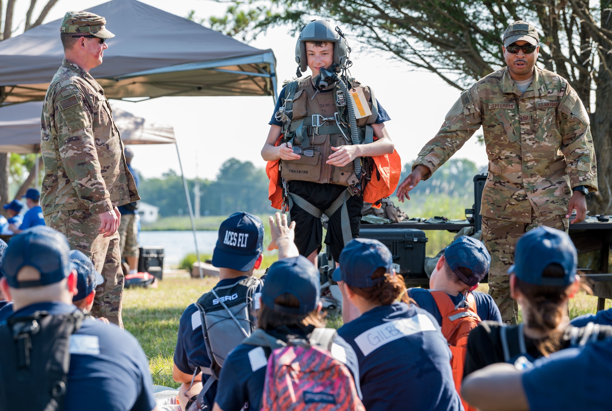 Tech. Sgts. Walter Norris, aircrew flight equipment craftsman, left, and Michael Jefferson, C-130H2 Hercules loadmaster, right, both members of the 142nd Airlift Squadron, New Castle Air National Guard Base, New Castle, Del., place aircrew flight equipment on Air Force Junior Reserve Officers’ Training Corps cadet Jonathan Bock of Aces Flight June 17, 2019, at the Delaware National Guard Bethany Beach Training Site, Bethany Beach, Del. Cadets participated in basic aircrew land survival skills training during the first two days of the six-day Cadet Leadership Course. (U.S. Air Force photo by Roland Balik)