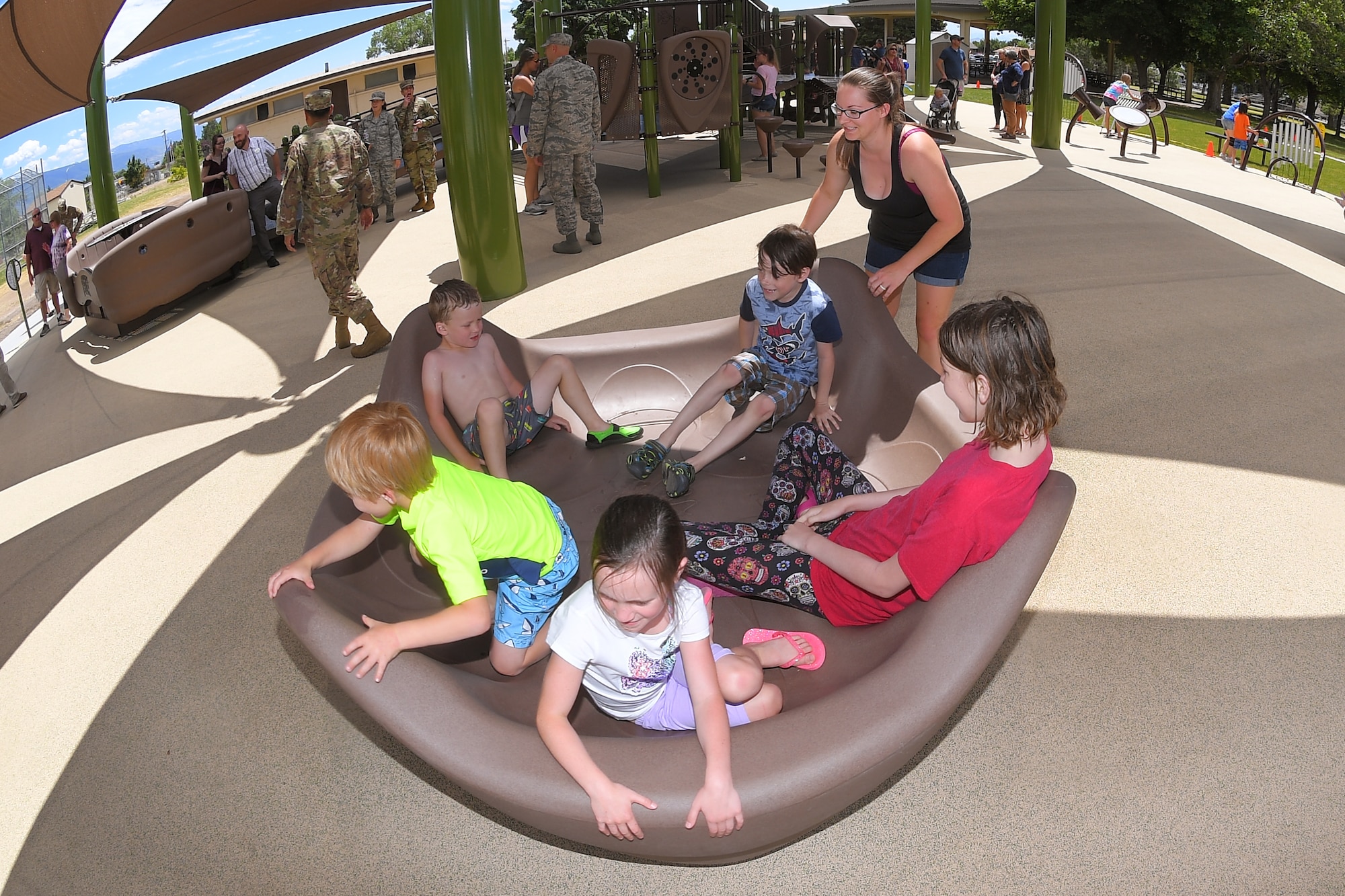 Rebecca McBride plays with children on the merry go-round at the new, all-abilities playground at Centennial Park June 24, 2019, at Hill Air Force Base, Utah. The playground is wheelchair accessible and incorporates sensory areas with a mixture of music- and texture-focused equipment for children. (U.S. Air Force photo by Todd Cromar)
