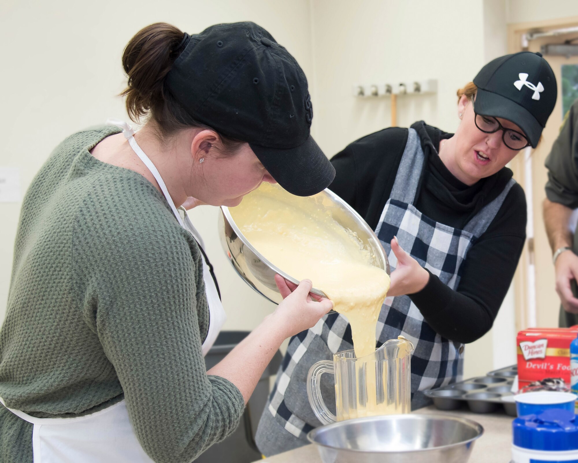 (Left to right) Brianna Wright and Cristy McDaniel, both volunteers, pour cake butter into a container the day before the fundraising bake sale at Yokota Air Base, Japan, Feb. 7, 2019.