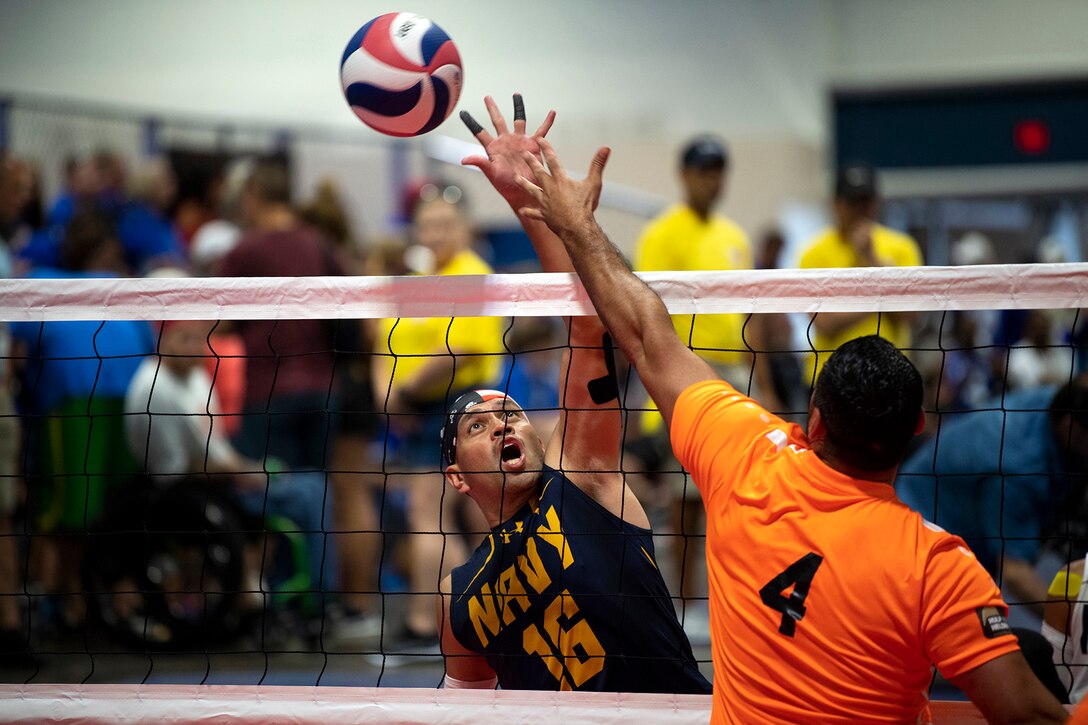 Two men compete for a volleyball over a net.