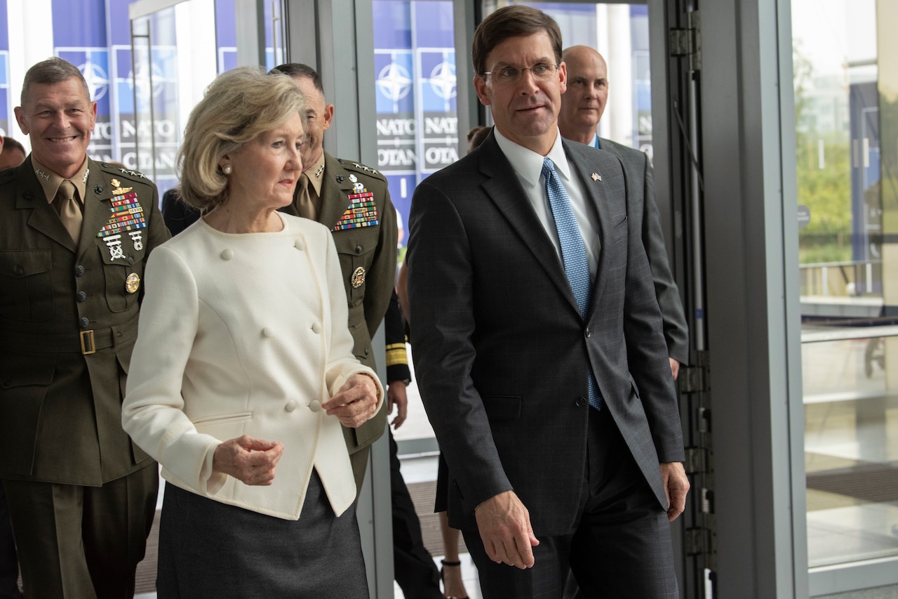 A woman and a man walk down a hall.