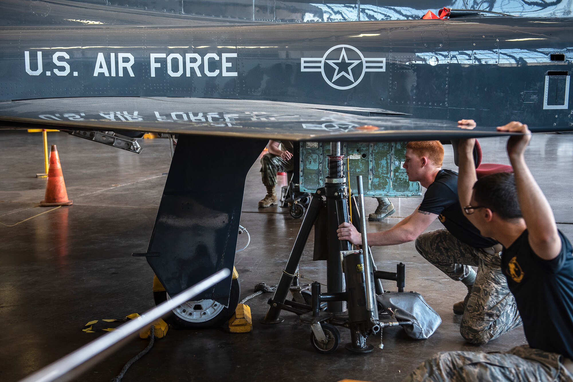 364th Training Squadron hydraulic systems apprentice course students positions an aircraft tripod jacks under a T-38 Talon at Sheppard Air Force Base, Texas, June 28, 2019. Each tripod jack requires at least two people and is manually operated. The students are lifting the jet to perform a gear swing operational check. (U.S. Air Force photo by Airman 1st Class Pedro Tenorio)