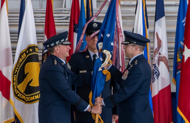 One person presenting a flag to another on a stage.