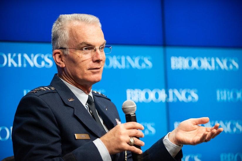 Two men talk, seated on stage with Brookings Institution backdrop.