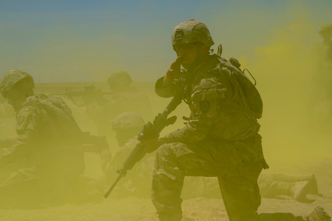 A soldier kneels down with a weapon in his hand surrounded by green smoke.