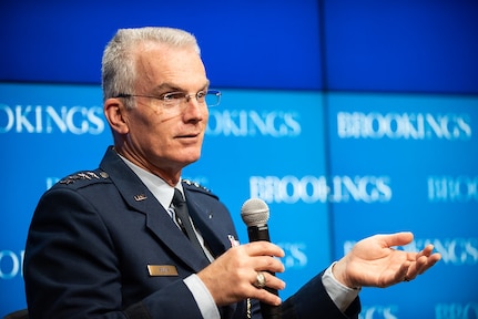 Two men talk, seated on stage with Brookings Institution backdrop.