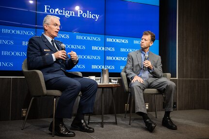 Two men talk, seated on stage with Brookings Institution backdrop.