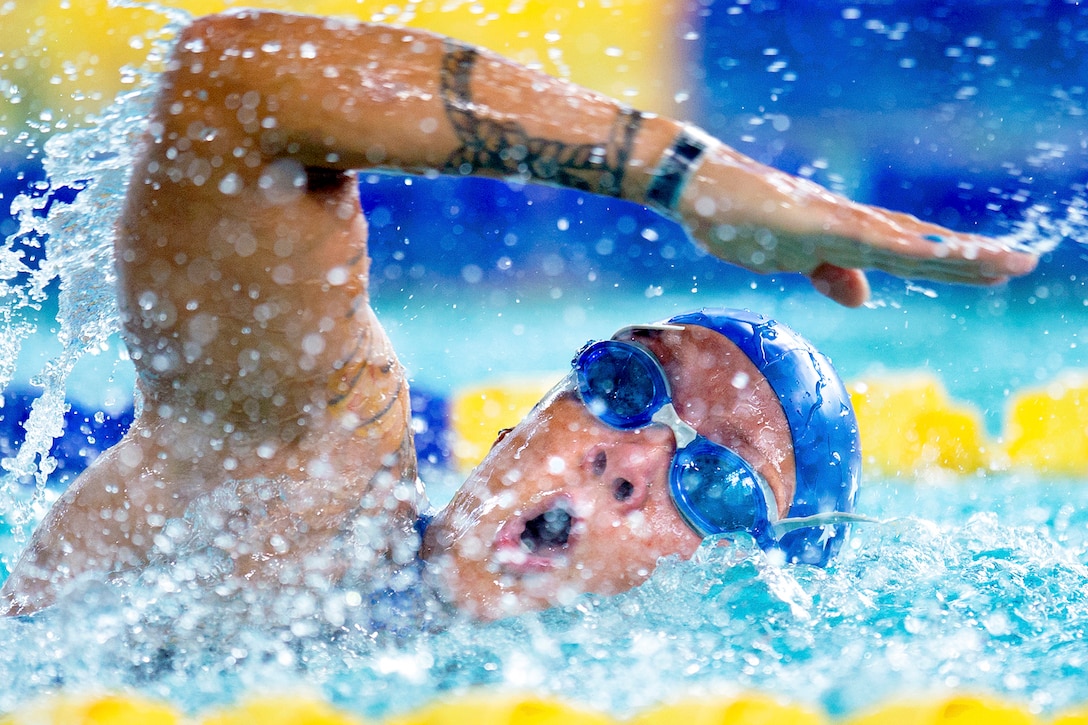 A swimmer moves arm through the air while swimming in a pool.