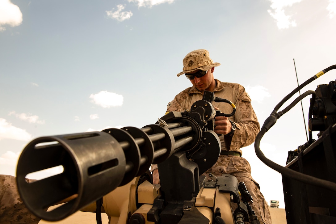 A Marine  holds onto and looks at down at a military vehicle's gun.