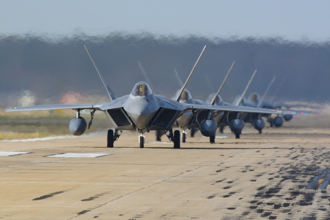 A line of F-22 Raptors sand by on the flightline.