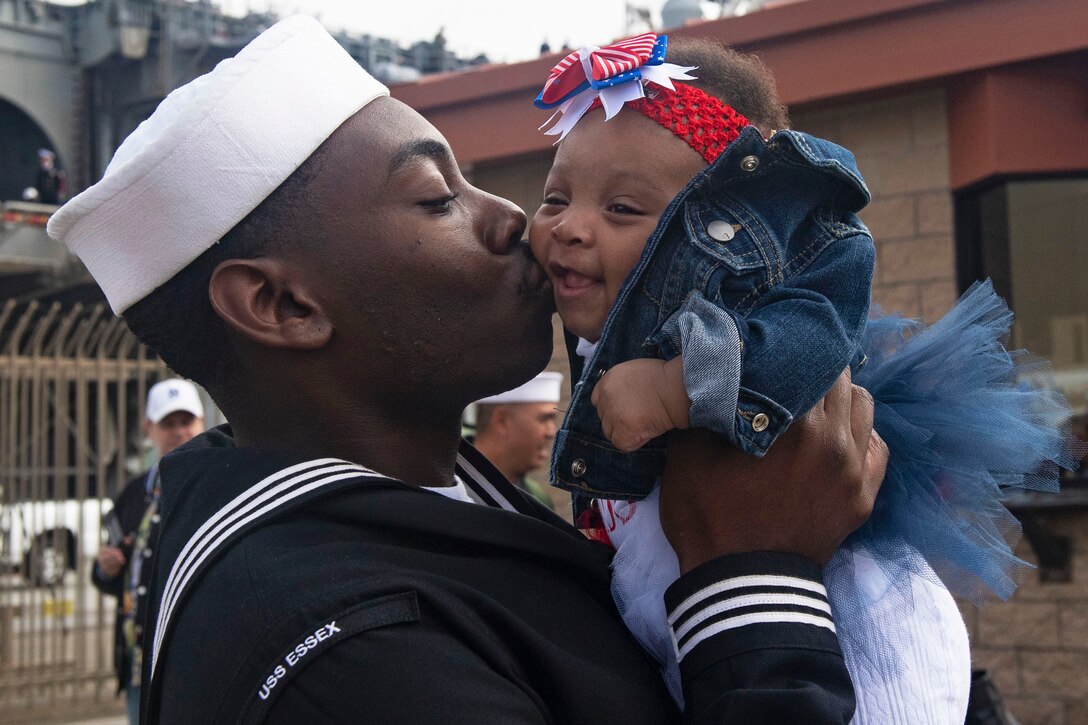 A sailor lifts and kisses his infant daughter.