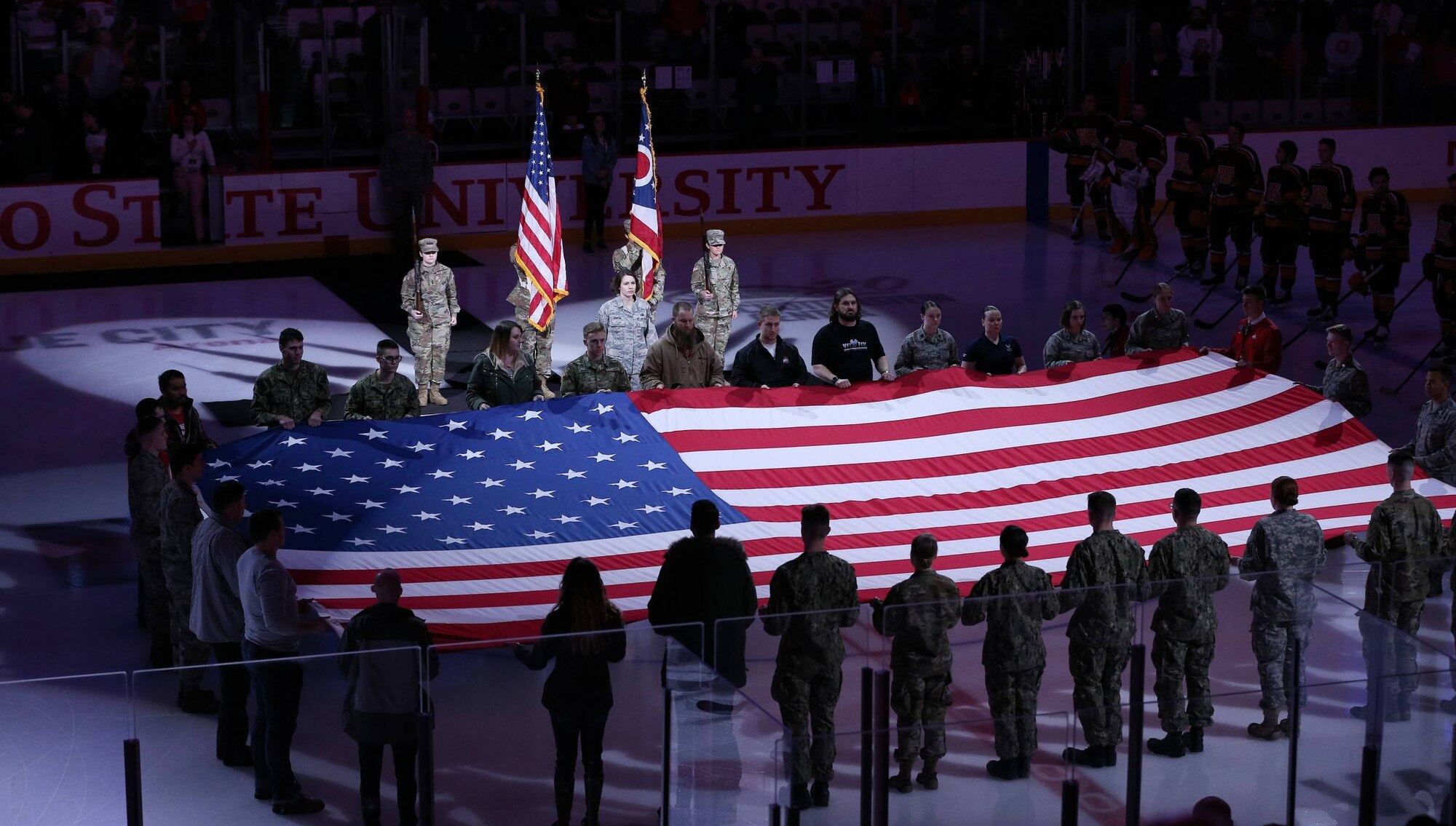 Air Force Band of Flight vocalist Staff Sgt. Joanne Griffin sings the National Anthem as members of Ohio State University Reserve Officer Training Corps units present the colors and hold a large U.S. flag over the ice during the pregame events at the Military Appreciation game between the Ohio State Buckeyes and the Minnesota Golden Gophers at the Value City Arena Schottenstein Center in Columbus, Ohio Feb. 15, 2019. The Buckeyes lost the game 3-4. (Courtesy Photo)
