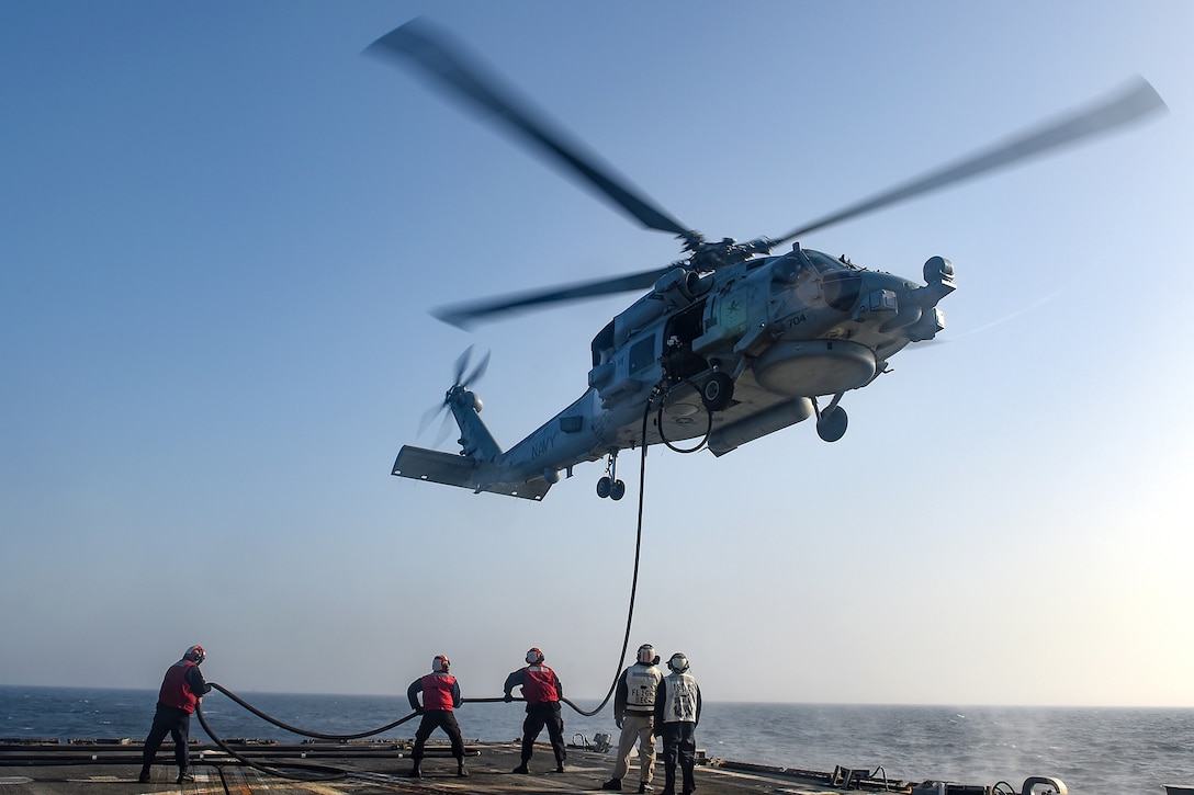 Sailors refuel a helicopter on a ship.