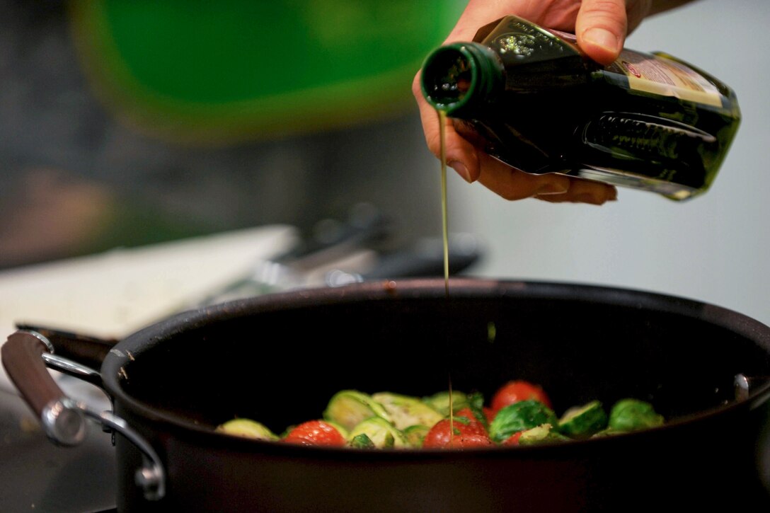 A hand pours olive oil from a bottle into a saucepan.