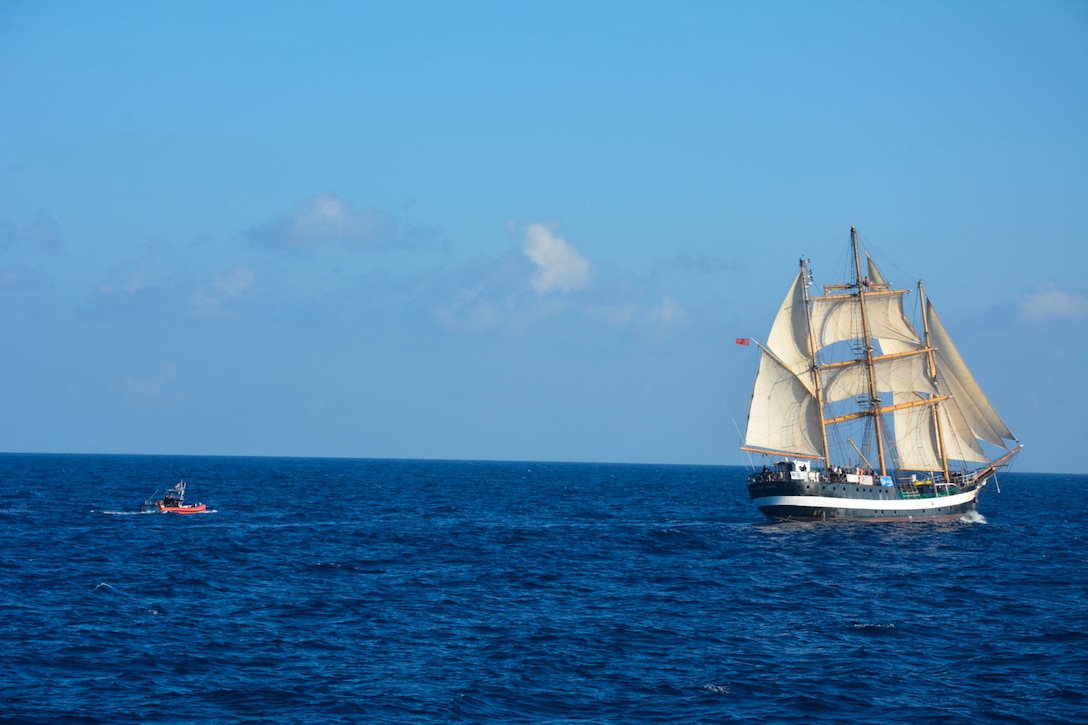 A small Coast Guard boat approaches a large sailing vessel in the middle of the water.