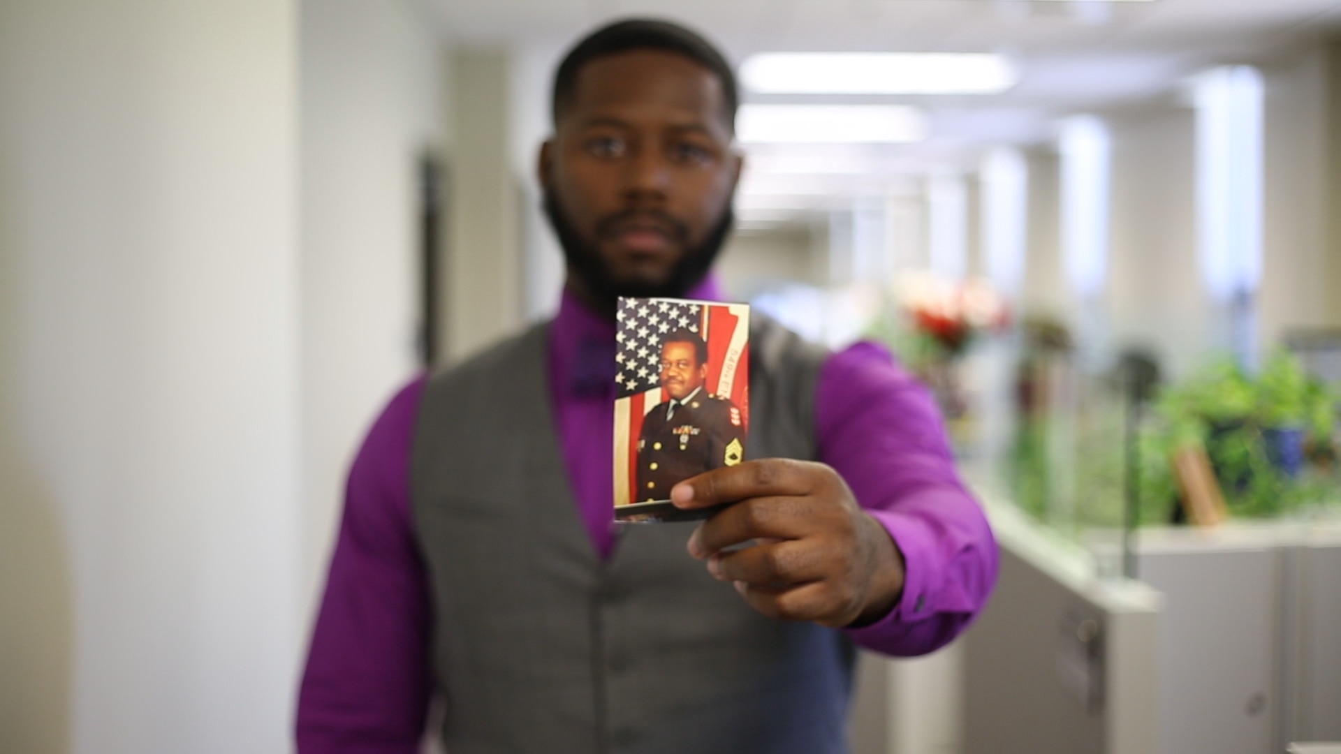 Man holds photo of another man in military uniform towards camera.