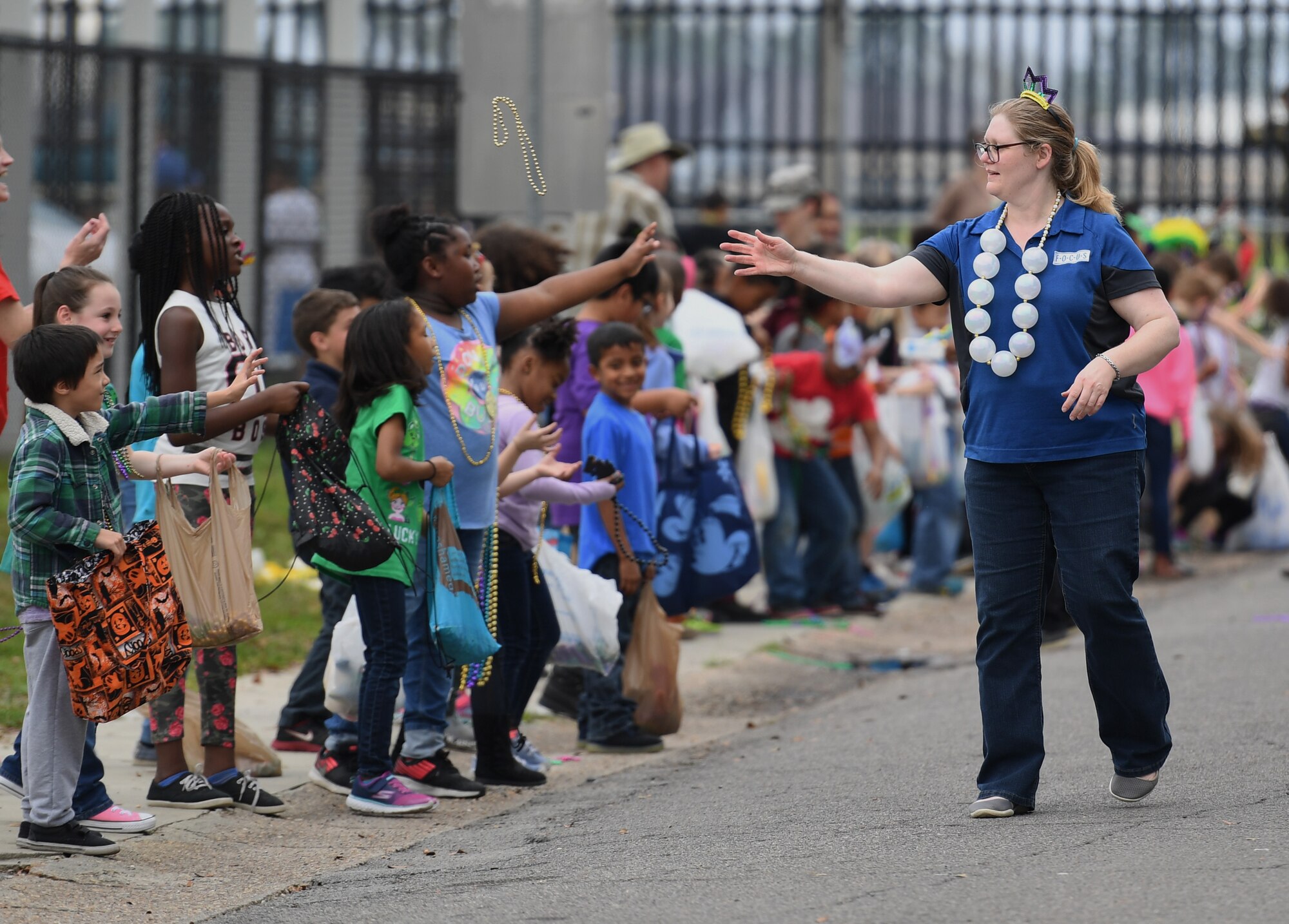 Diane Cook, Families Overcoming Under Stress (FOCUS) resilience trainer, tosses beads to children during the Jeff Davis Elementary School Mardi Gras parade in Biloxi, Mississippi, March 1, 2019. Keesler leadership, Honor Guard and Airmen participated in various festivities throughout the Mardi Gras season, which is celebrated by the local communities. (U.S. Air Force photo by Kemberly Groue)