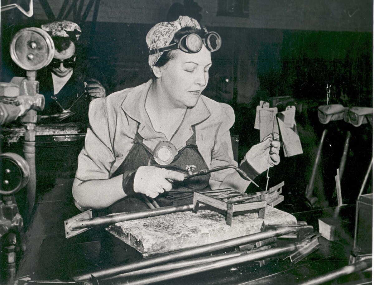 Two women weld sitting at tables.