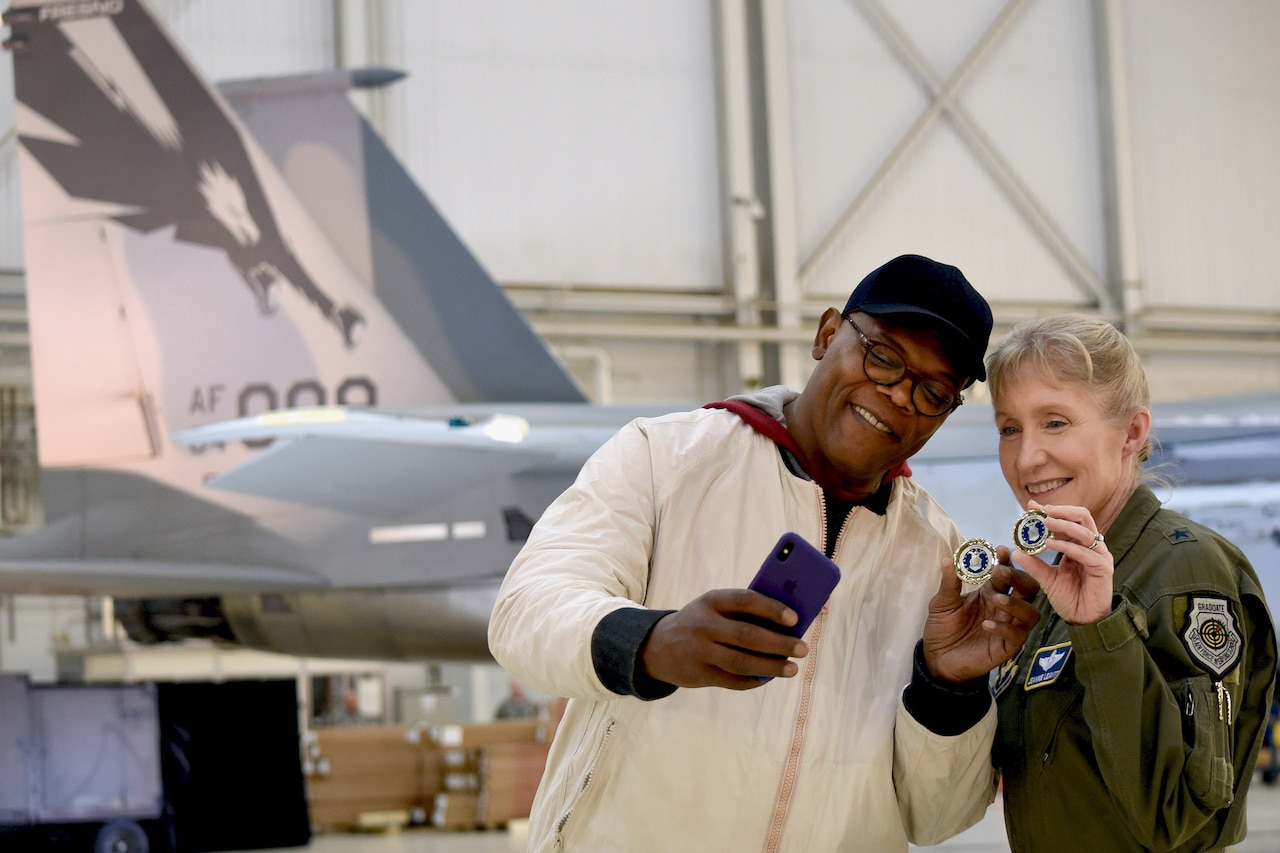 Actor takes photo with airman and challenge coin.