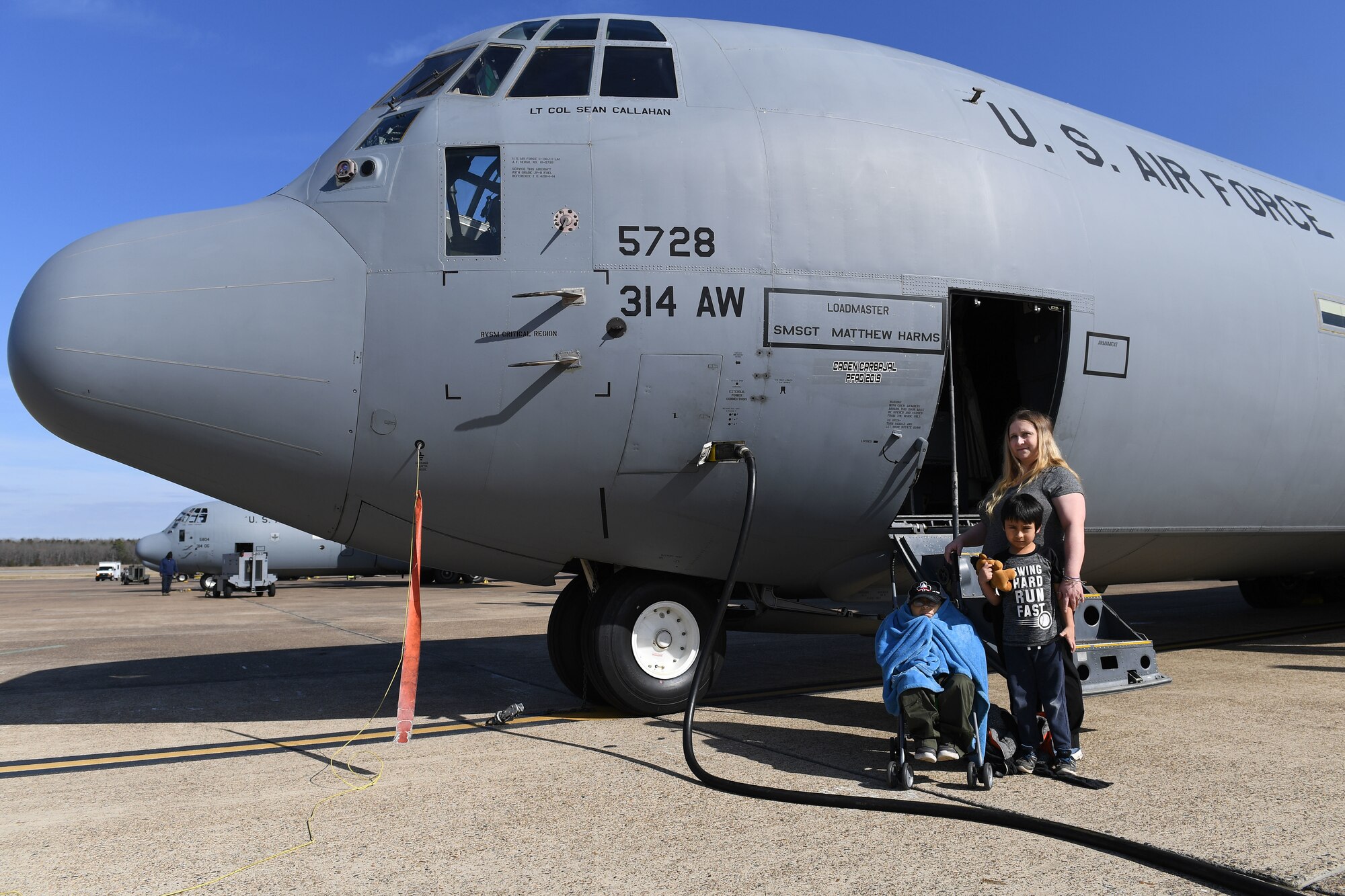 A mother and her two sons pose for a photo on the flight line in front of a C-130J airplane.