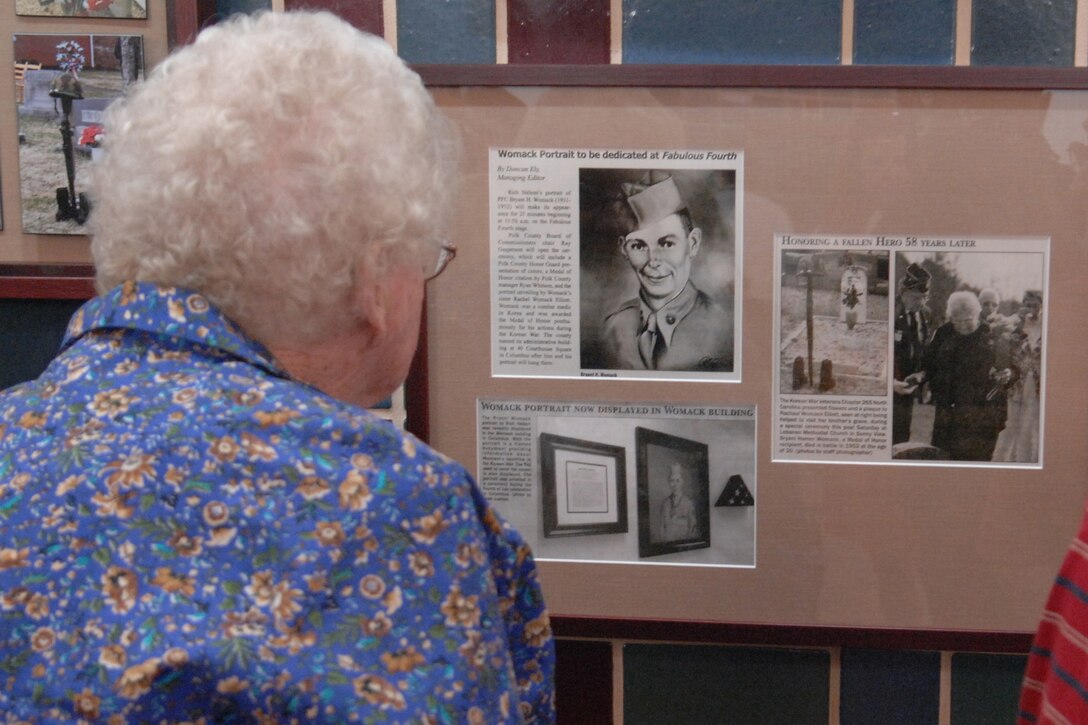 An older woman looks at a group of pictures on a bulletin board.