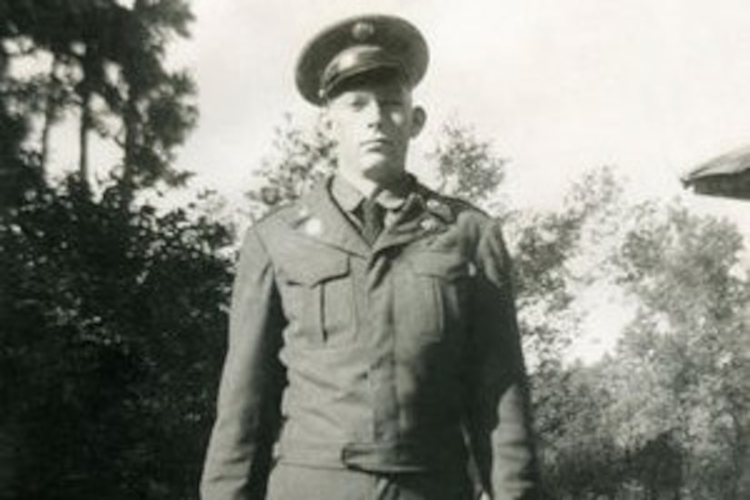 A soldier stands in a field in uniform.