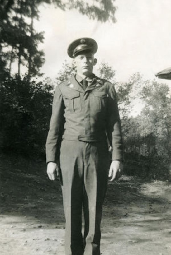 A soldier stands in a field in uniform.