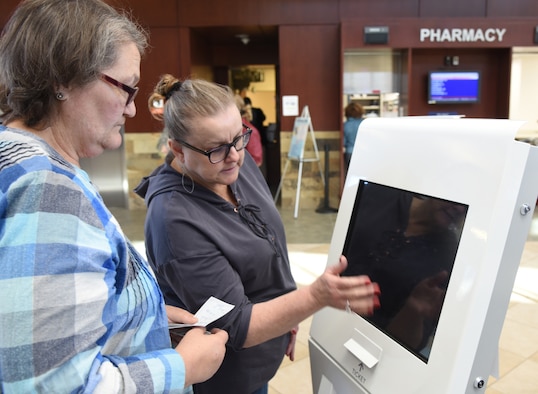 Teresa Larios, pharmacy technician with the 72nd Medical Support Squadron, assists a pharmacy customer with one of the new Q-Flow machines inside the lobby of the 72nd Medical Group. The Q-Flow kiosks allow pharmacy customers to check-in to pick up their prescriptions and will show them on the large screens in the waiting area what their wait time is. (U.S. Air Force photo/Kelly White)