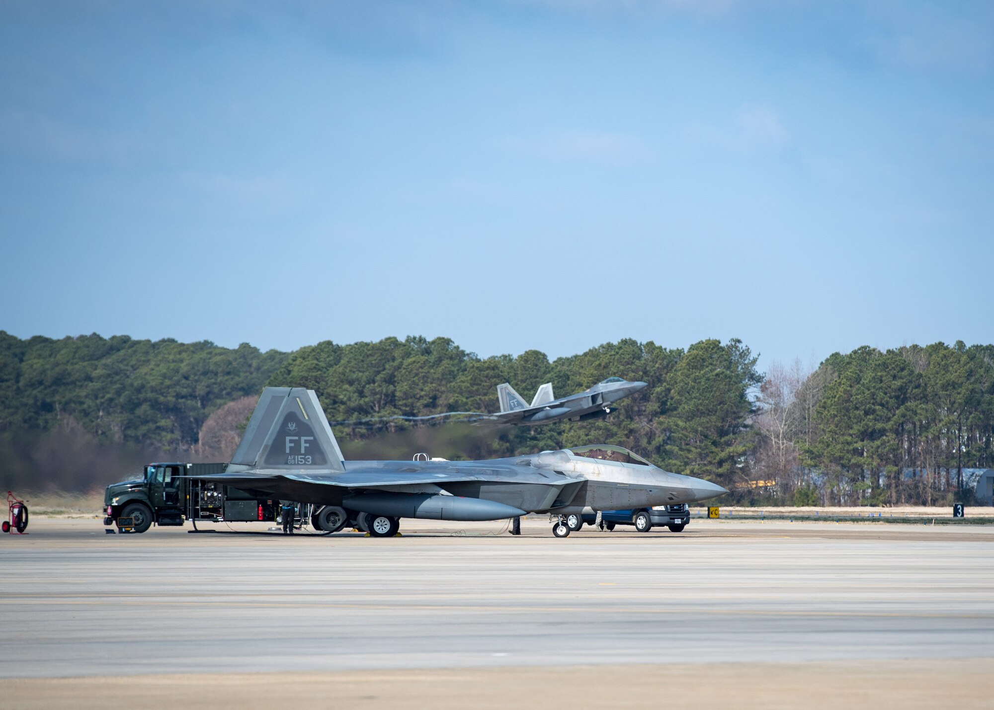 The 733rd Logistics Readiness Squadron fuels flight refuels a U.S. Air Force F-22 Raptor  while another F-22 takes off during a total force exercise at Joint Base Langley-Eustis, Virginia, Feb. 28, 2019.